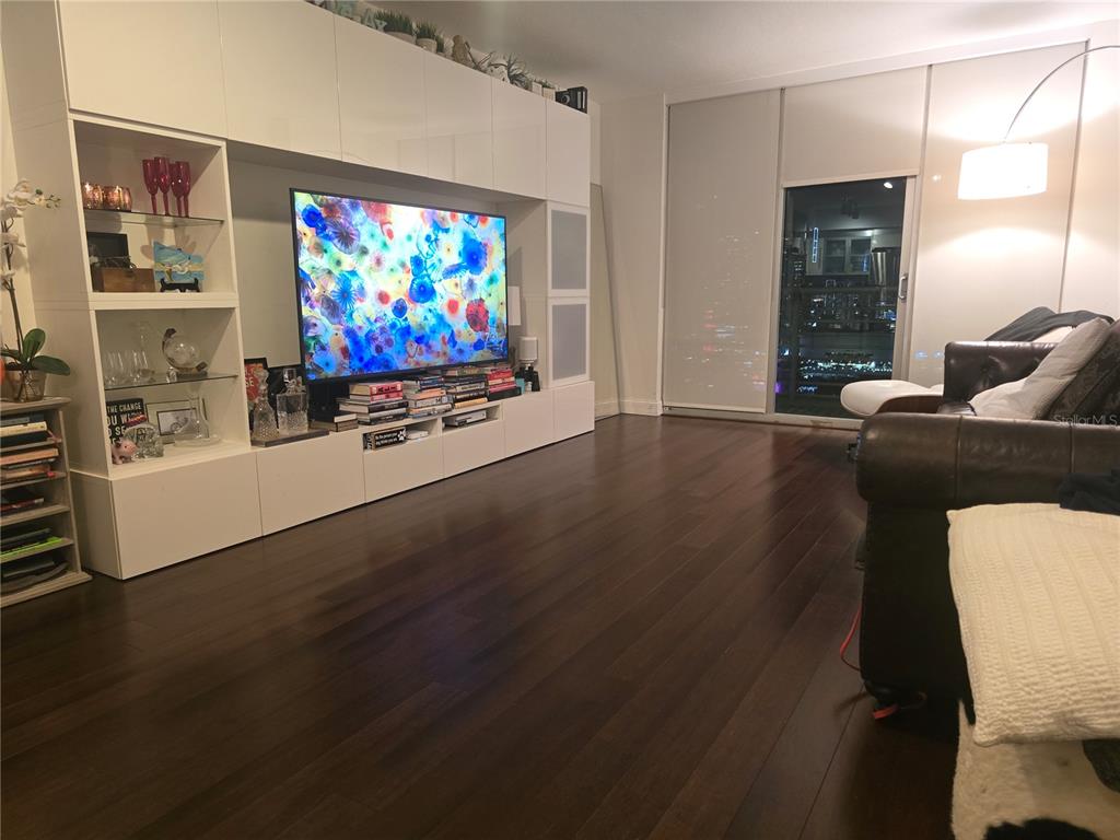 A living room features dark hardwood floors, a large white wall unit, and a television — 335 S BISCAYNE BOULEVARD UNIT 3400, MIAMI, FL