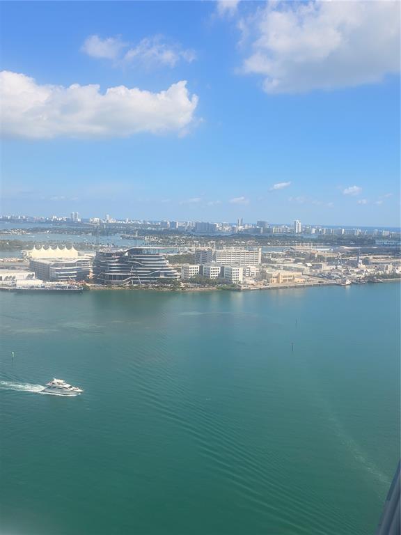 An aerial view of a waterfront cityscape featuring a modern building and a passing yacht — 335 S BISCAYNE BOULEVARD UNIT 3400, MIAMI, FL
