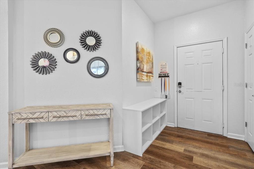 An entryway features a wood console table, white cubby storage, wall mirrors, and wood flooring — 4126 BREAKVIEW DRIVE UNIT 40601, ORLANDO, FL