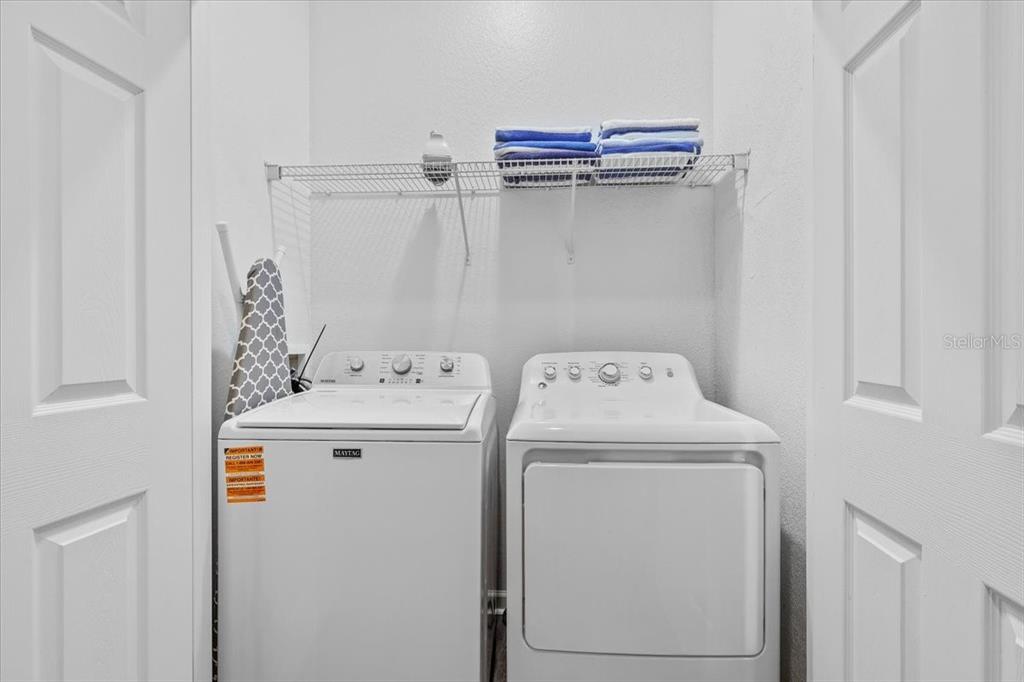A laundry closet features a white top-load washer and dryer with a wire storage shelf above — 4126 BREAKVIEW DRIVE UNIT 40601, ORLANDO, FL