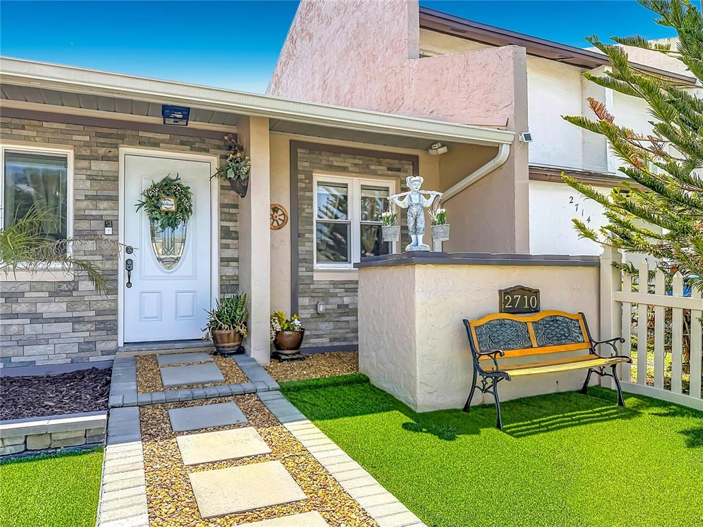 A front entrance features a stone-accented facade, a white door, and a bench on artificial turf — 2710 CHARING CROSS WAY, ORLANDO, FL