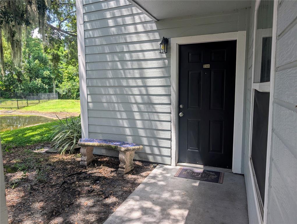 A black front door with a small bench sits on a concrete porch beside siding — 2550 N ALAFAYA TRAIL UNIT 12105, ORLANDO, FL