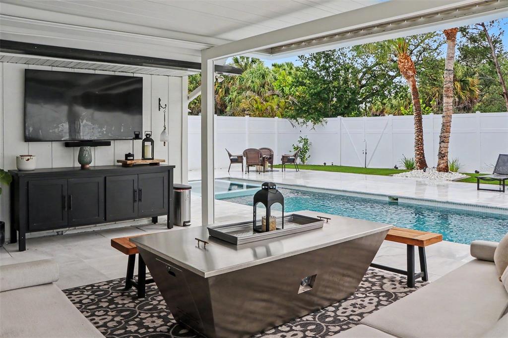 A covered patio features a fire pit, seating, a television, and a swimming pool — 5143 SANDY BEACH AVENUE, SARASOTA, FL