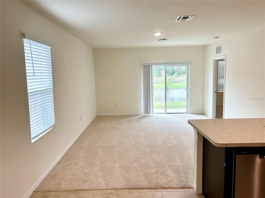 A carpeted living room features a sliding glass door with a view of a pond — 3349 COSTELLO CIRCLE, WINTER HAVEN, FL