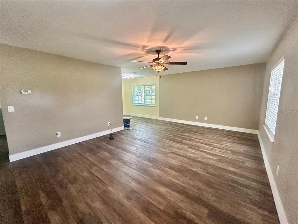 An empty living room features wood-look flooring, beige walls, a ceiling fan, and a window — 770 SW 125TH AVENUE, OCALA, FL