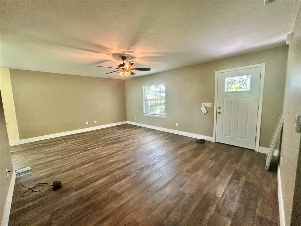An empty room features wood-look flooring, beige walls, a ceiling fan, and a front door — 770 SW 125TH AVENUE, OCALA, FL