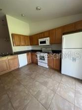 A kitchen features light wood cabinets, white appliances, dark countertops, and tile flooring — 6 WOOD AMBER LANE UNIT B, PALM COAST, FL