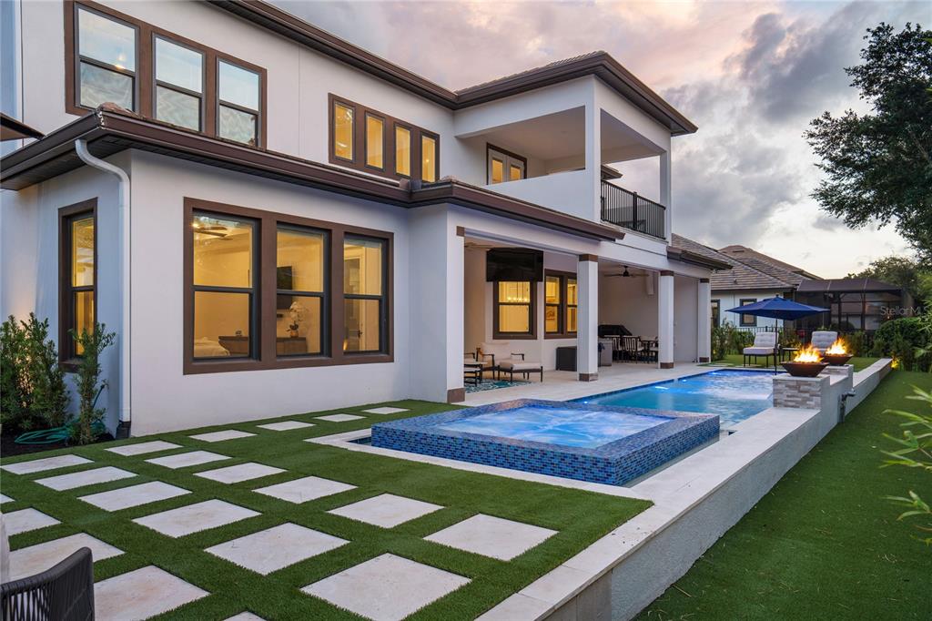 A two-story house exterior features a backyard pool, spa, and artificial turf with stone pavers — 10175 BROCKSPORT CIRCLE, GOTHA, FL