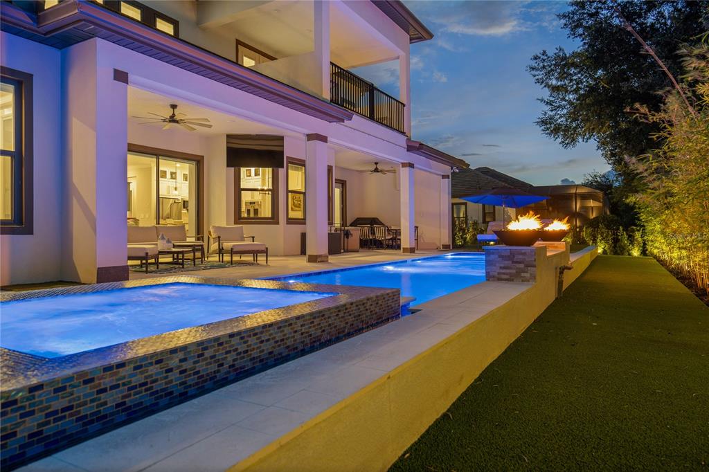 An illuminated swimming pool and spa sit on a patio beside a two-story modern home — 10175 BROCKSPORT CIRCLE, GOTHA, FL