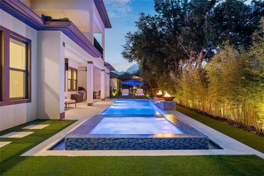 A modern backyard features a rectangular swimming pool with an attached raised spa and fire bowls — 10175 BROCKSPORT CIRCLE, GOTHA, FL