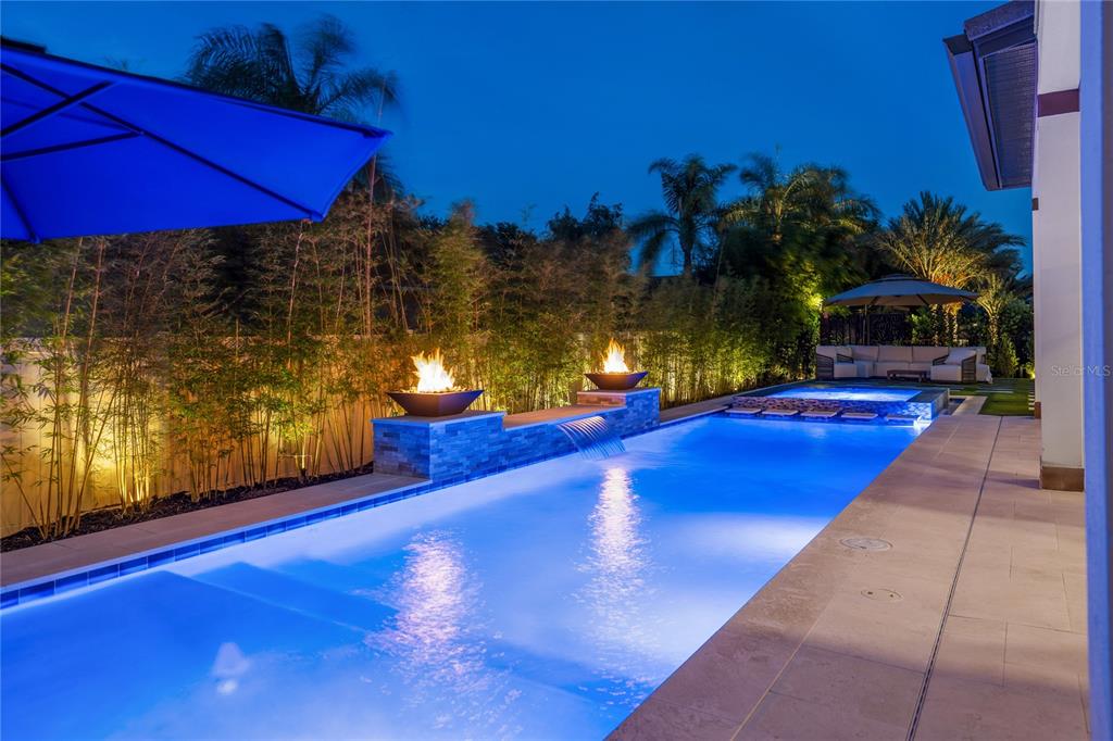 A rectangular swimming pool with a water feature, fire bowls, and a spa at dusk — 10175 BROCKSPORT CIRCLE, GOTHA, FL