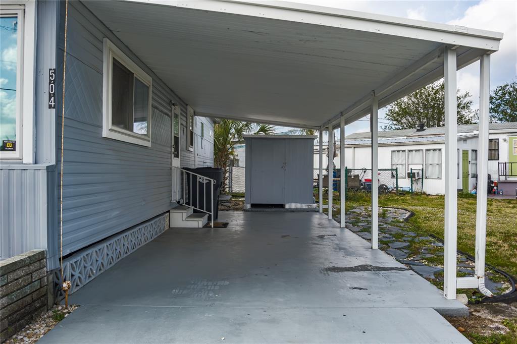 A gray mobile home features a covered carport with a concrete floor and storage shed — 504 50TH AVENUE DR W, BRADENTON, FL