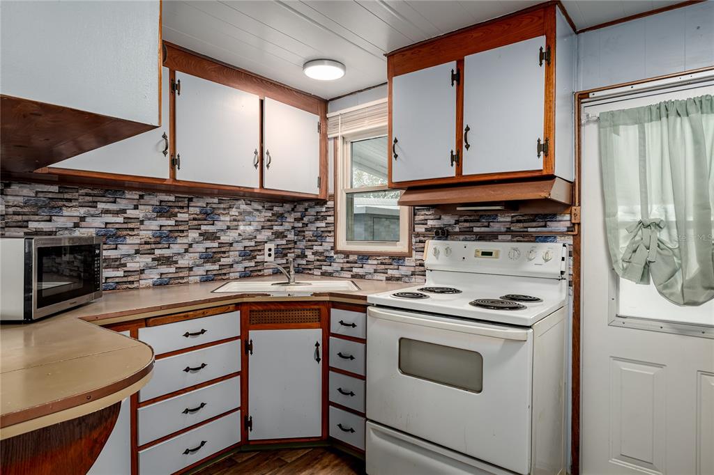 A kitchen with white cabinets, a stone-patterned backsplash, a white stove, and a corner sink — 504 50TH AVENUE DR W, BRADENTON, FL