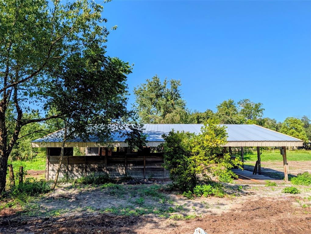 A wooden horse barn with a metal roof stands in a grassy, partially shaded field — 21320 SENECA HILLS ROAD, EUSTIS, FL