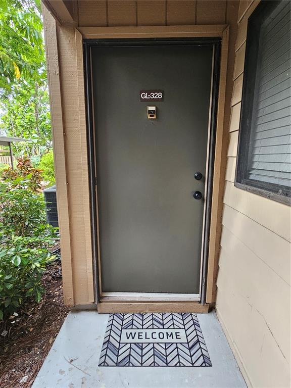 A gray front door with a welcome mat is set within a tan exterior wall — 1720 GLENHOUSE DRIVE UNIT 328, SARASOTA, FL