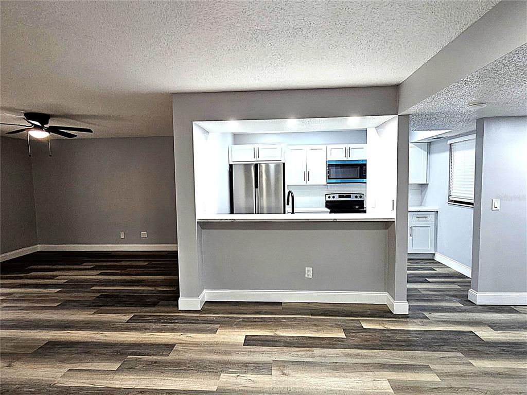 A kitchen with stainless steel appliances and white cabinets overlooks a living area with wood-look flooring — 1720 GLENHOUSE DRIVE UNIT 328, SARASOTA, FL