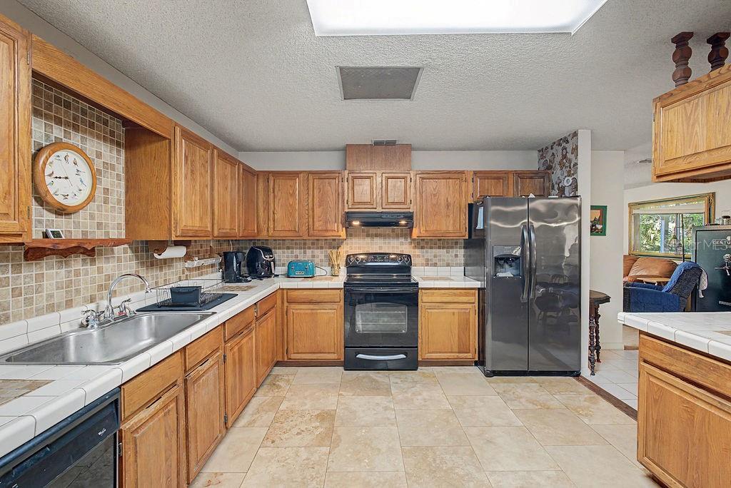 A kitchen featuring oak cabinets, tile countertops, a stainless steel refrigerator, and a tiled floor — 12960 SE 114TH PLACE, DUNNELLON, FL