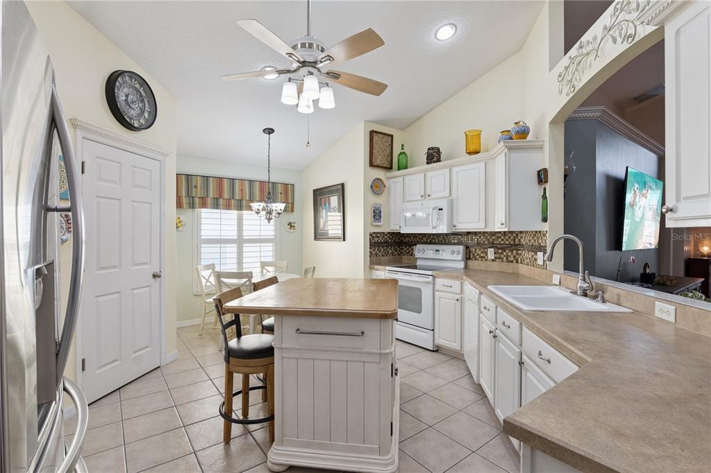 A kitchen with white cabinets, a wooden island, tile floors, and an adjacent dining area — 9943 HERON POINTE DRIVE, ORLANDO, FL