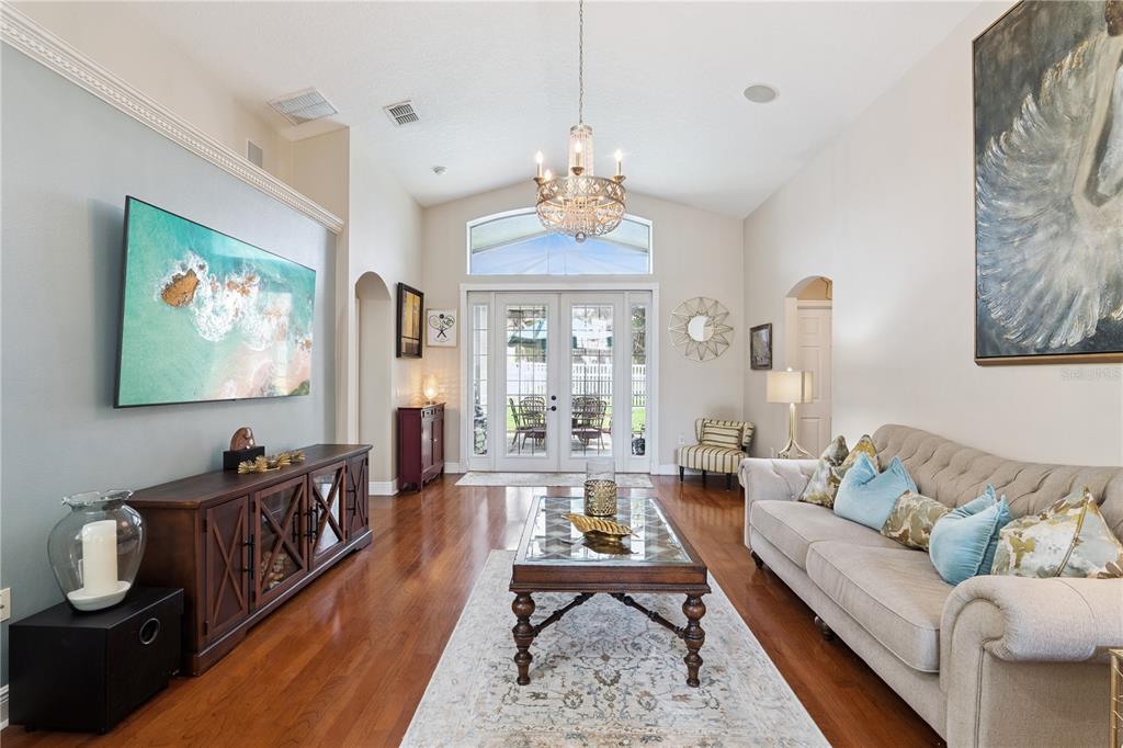A living room features hardwood floors, a tufted sofa, a chandelier, and double glass doors — 9943 HERON POINTE DRIVE, ORLANDO, FL