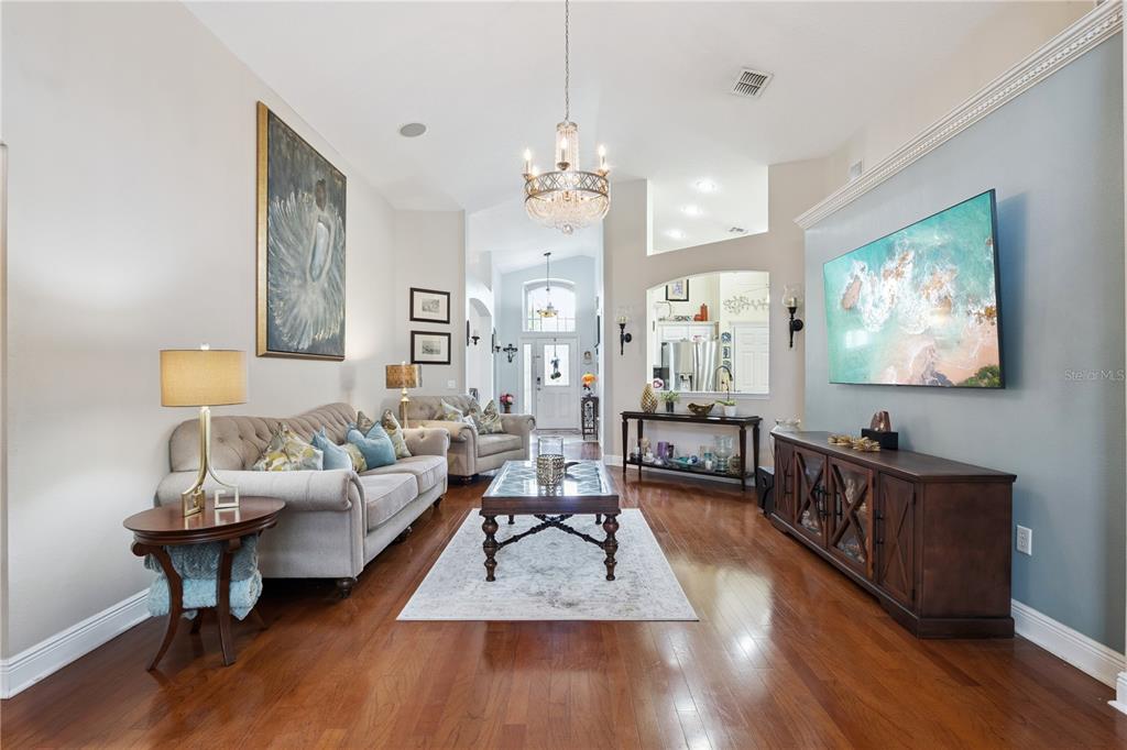 A living room features hardwood floors, a tufted sofa, a chandelier, and a wall-mounted television — 9943 HERON POINTE DRIVE, ORLANDO, FL