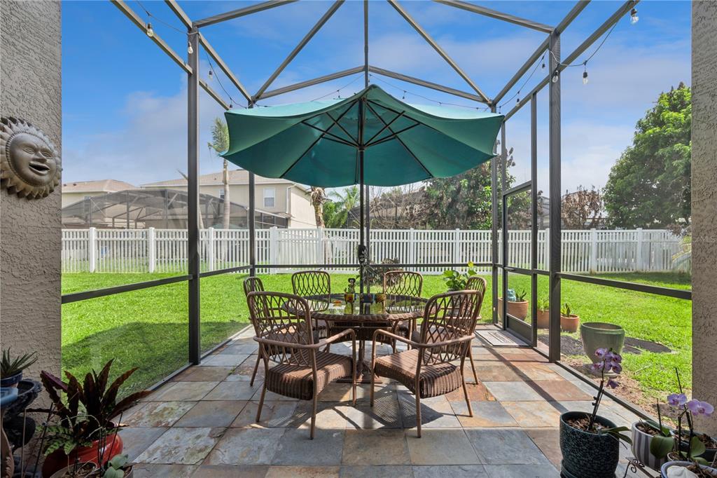 A screened-in patio features a dining set under a teal umbrella on a tiled floor — 9943 HERON POINTE DRIVE, ORLANDO, FL