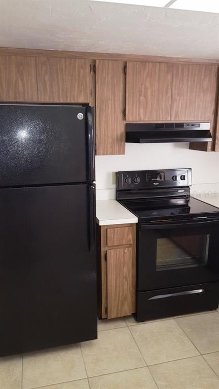 A kitchen features wood-grain cabinets, black appliances, and light-colored tile flooring — 4600 98TH WAY N UNIT 306, ST PETERSBURG, FL