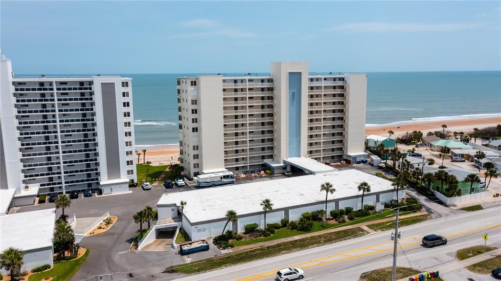 An aerial view shows two high-rise apartment buildings near a beach with a parking lot — 1133 OCEAN SHORE BOULEVARD UNIT 302, ORMOND BEACH, FL
