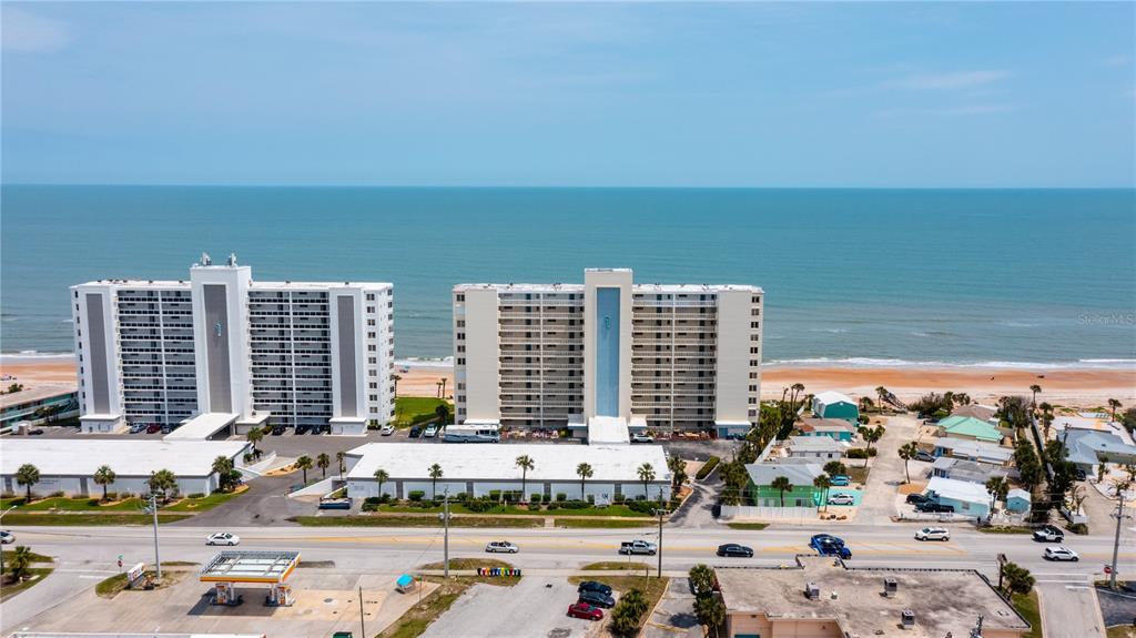 An aerial view shows two tall beachfront apartment buildings near a road and a gas station — 1133 OCEAN SHORE BOULEVARD UNIT 302, ORMOND BEACH, FL