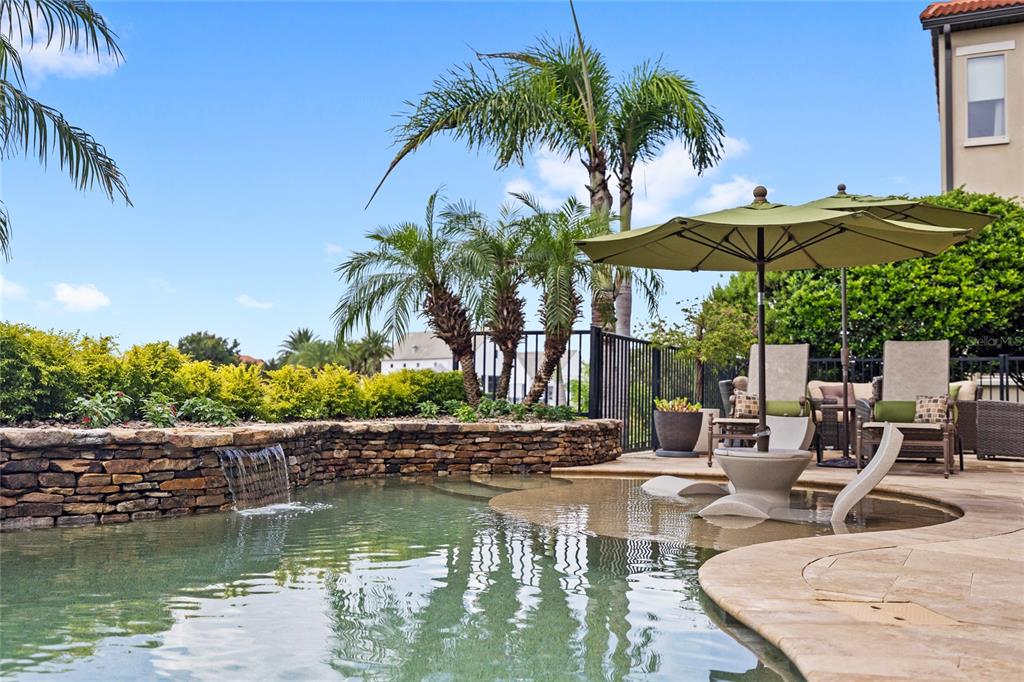 A swimming pool with a stone waterfall feature and a patio area with lounge chairs — 15475 SHOREBIRD LANE, WINTER GARDEN, FL