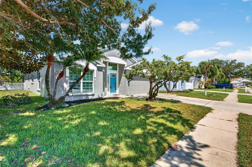 A single-story gray house with a blue front door and a palm tree in front — 4623 SANIBEL WAY, BRADENTON, FL