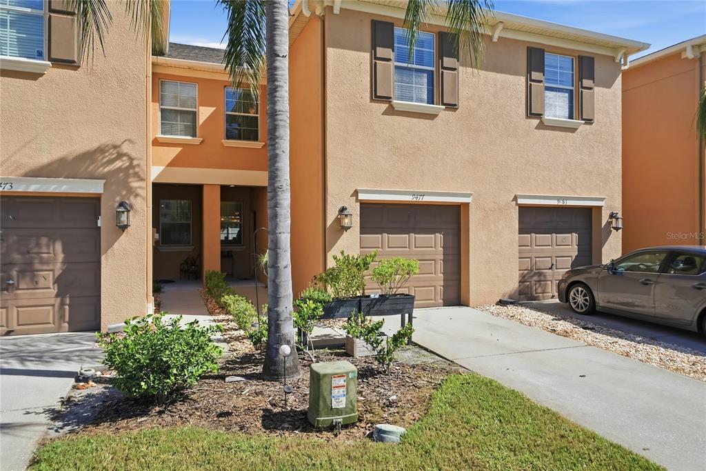 An exterior view of a multi-unit townhouse complex with tan stucco walls and brown garages — 9477 TRUMPET VINE LOOP, TRINITY, FL