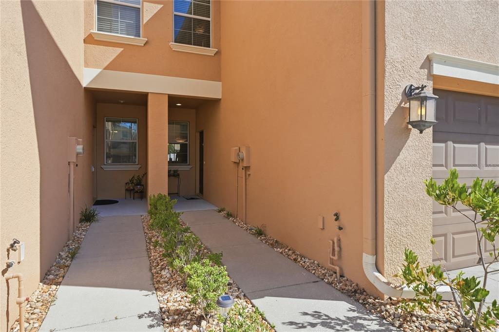 A tan stucco townhouse exterior features two parallel walkways leading to recessed front entry doors — 9477 TRUMPET VINE LOOP, TRINITY, FL