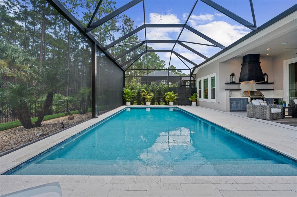 A rectangular swimming pool sits inside a screened-in patio with an outdoor kitchen area — 463 STIRLING BRIDGE DRIVE, ORMOND BEACH, FL