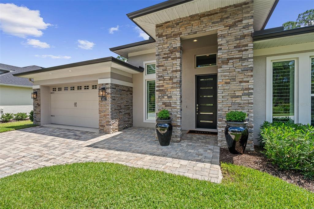 A modern house exterior features a stone-clad entryway, a garage, and a paved driveway — 463 STIRLING BRIDGE DRIVE, ORMOND BEACH, FL
