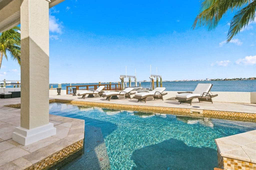 A swimming pool sits on a patio overlooking a bay with lounge chairs and docks — 504 55 TH AVENUE, ST PETE BEACH, FL