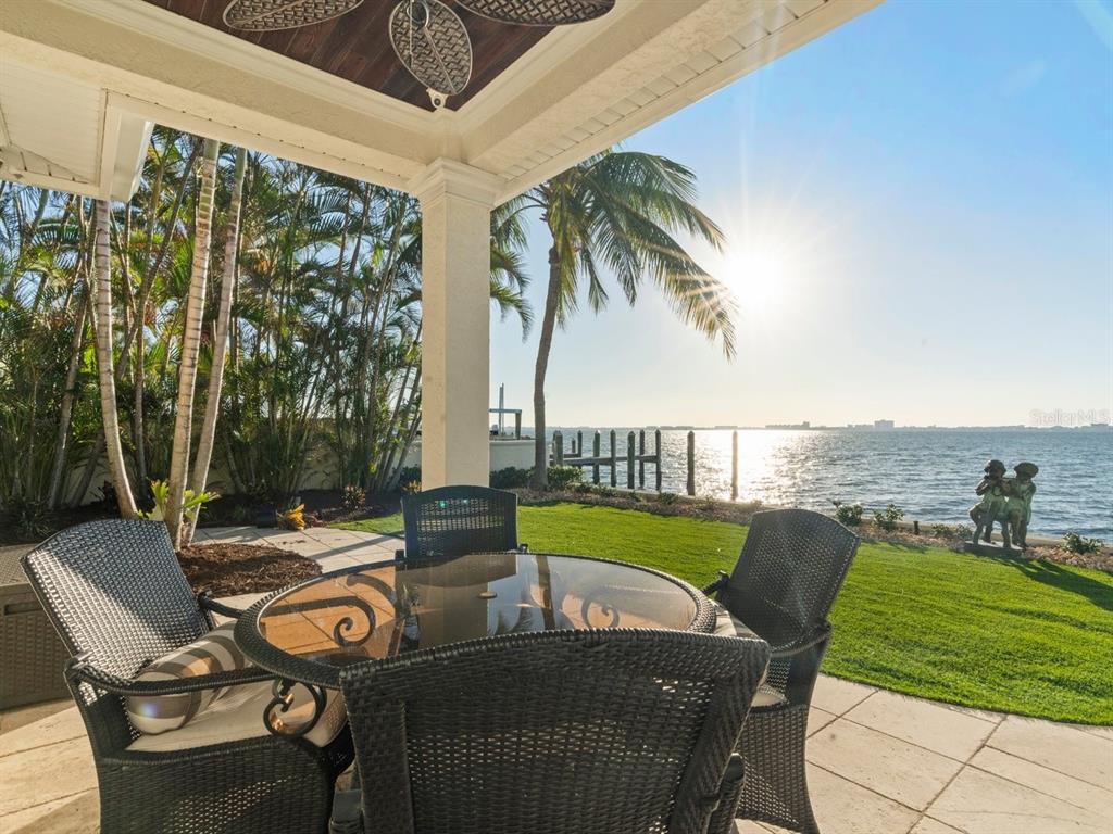 A patio with wicker furniture overlooks a grassy lawn, palm trees, and a waterfront view — 504 55 TH AVENUE, ST PETE BEACH, FL