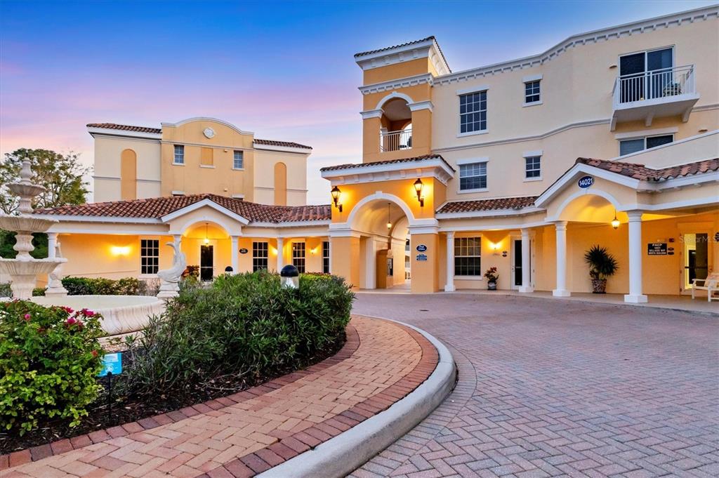 A multi-story stucco building with a brick driveway, arched entryways, and a front fountain — 14041 BELLAGIO WAY UNIT 214, OSPREY, FL