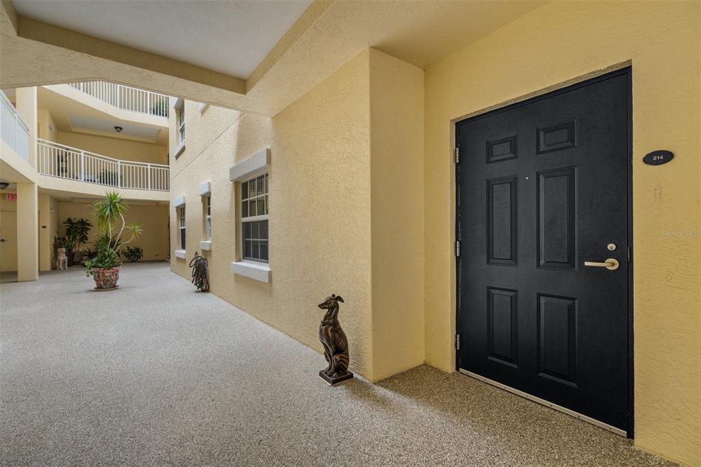 A dark front door with the number 214 sits in a yellow-walled outdoor corridor — 14041 BELLAGIO WAY UNIT 214, OSPREY, FL