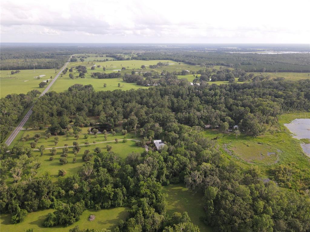 An aerial view shows a house surrounded by trees, open fields, and a nearby lake — 15208 SW WILLISTON RD, MICANOPY, FL