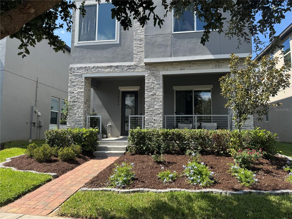 A two-story house exterior features a stone facade, a brick walkway, and a front porch — 10439 AUSTRINA OAK LOOP, WINTER GARDEN, FL