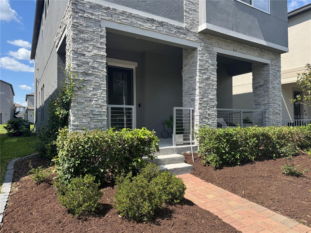 The exterior of a modern house features a stone-clad porch with metal railings and landscaping — 10439 AUSTRINA OAK LOOP, WINTER GARDEN, FL