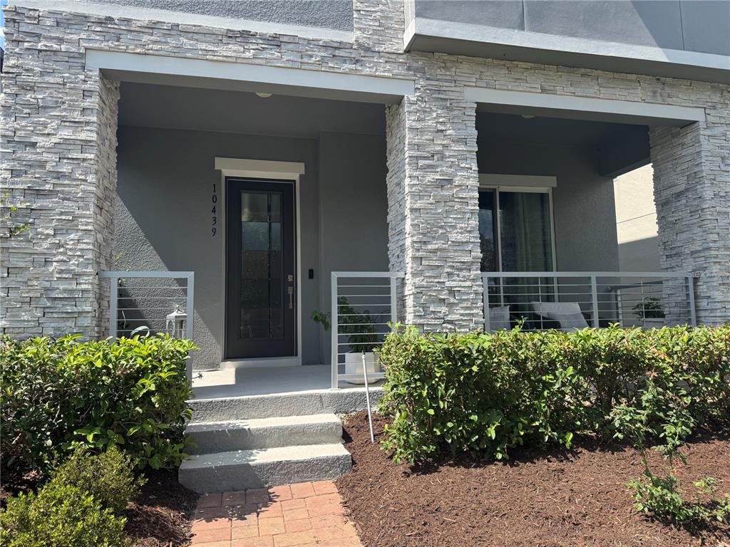 The front entrance of a house features stone pillars, a dark door, and metal railings — 10439 AUSTRINA OAK LOOP, WINTER GARDEN, FL