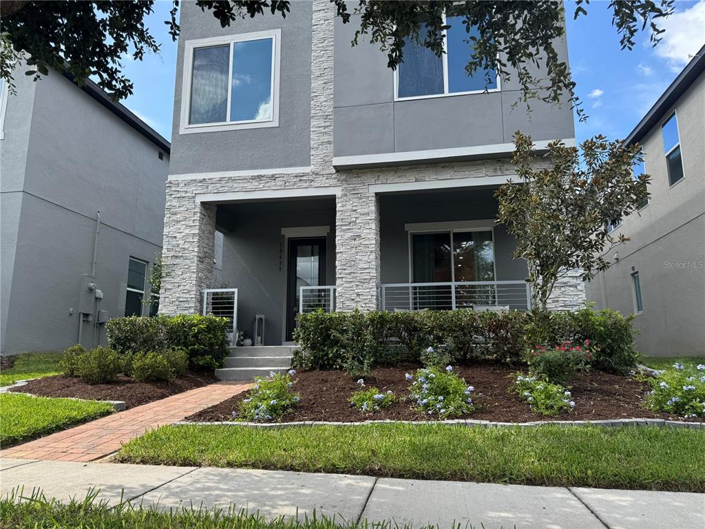 A two-story house exterior features a stone-accented facade, a front porch, and a landscaped yard — 10439 AUSTRINA OAK LOOP, WINTER GARDEN, FL