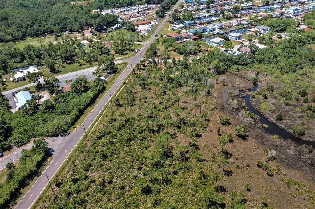 An aerial view shows a wooded lot adjacent to a road and a nearby residential neighborhood — 00 GULF WAY, HUDSON, FL