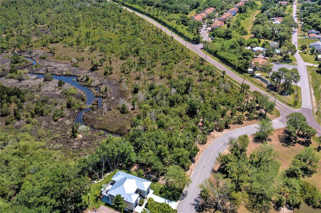 An aerial view shows a house, a winding creek, and surrounding wooded land near roads — 00 GULF WAY, HUDSON, FL