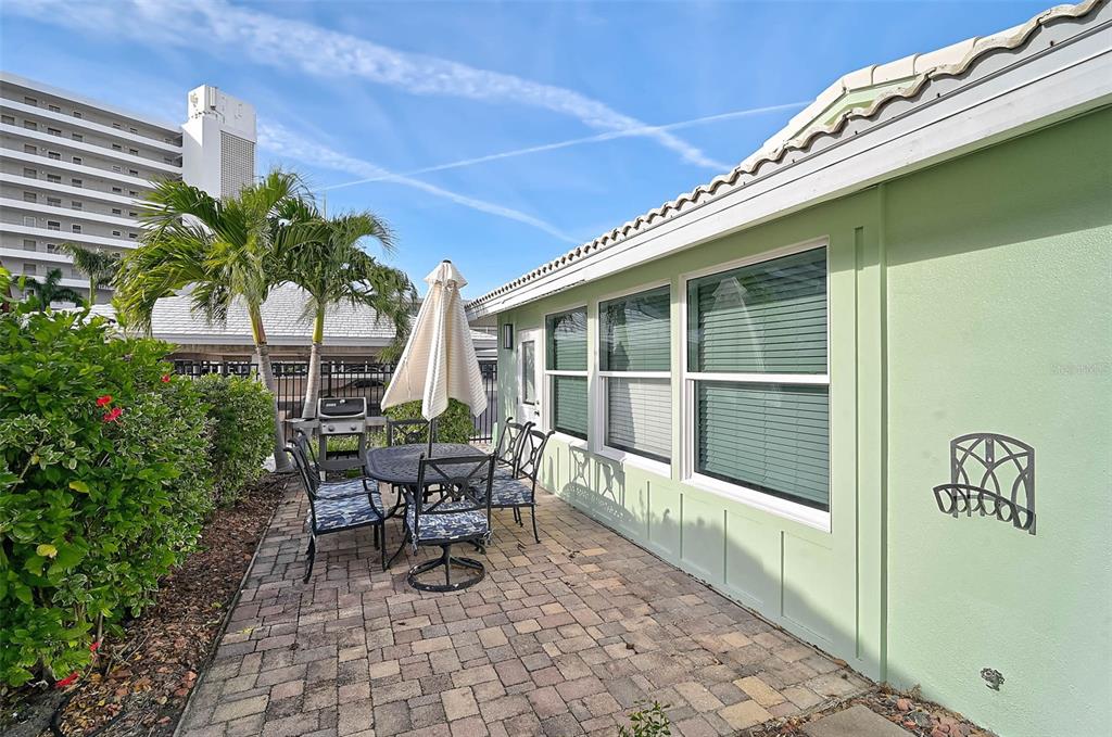 A paved patio with outdoor furniture sits beside a light green house with large windows — 6308 MIDNIGHT PASS ROAD UNIT 6, SARASOTA, FL