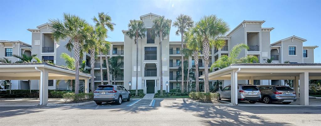A multi-story apartment building features covered parking structures in the foreground and palm trees — 17510 GAWTHROP DRIVE UNIT 308, BRADENTON, FL
