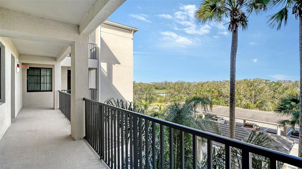 An outdoor balcony with a black metal railing overlooks a parking area and wooded landscape — 17510 GAWTHROP DRIVE UNIT 308, BRADENTON, FL