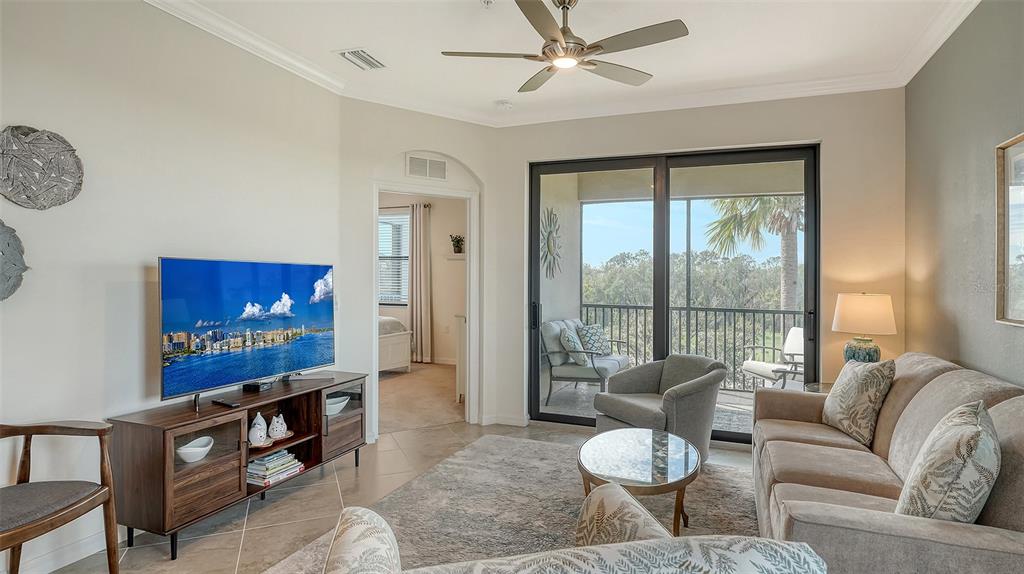 A living room features a television, sofa, armchairs, and a sliding door to a balcony — 17510 GAWTHROP DRIVE UNIT 308, BRADENTON, FL