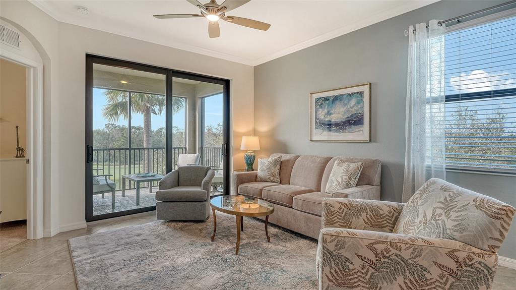 A living room features a beige sofa, patterned armchair, glass coffee table, and sliding glass doors — 17510 GAWTHROP DRIVE UNIT 308, BRADENTON, FL